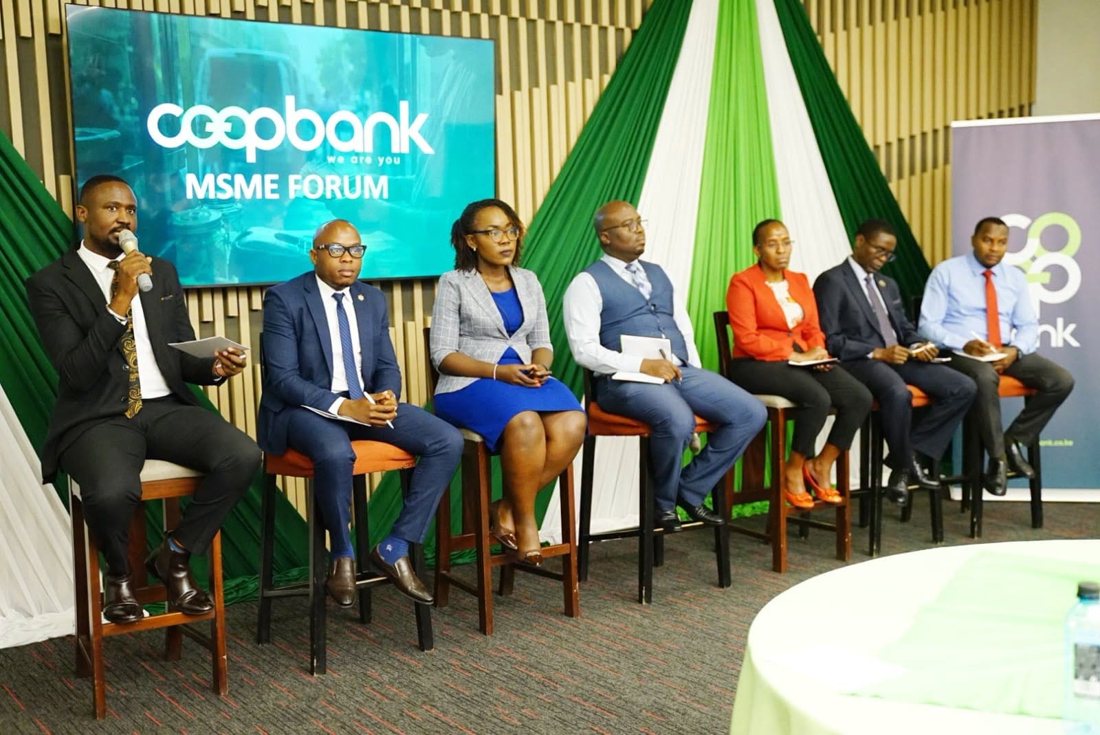 Co op Bank representatives seated on a panel at an MSME Forum, with the bank’s branding and green and white event decorations behind them.